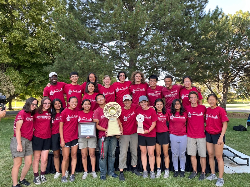 22 students wearing red S.E.V.T. shirts stand in two rows, holding their trophy in front
